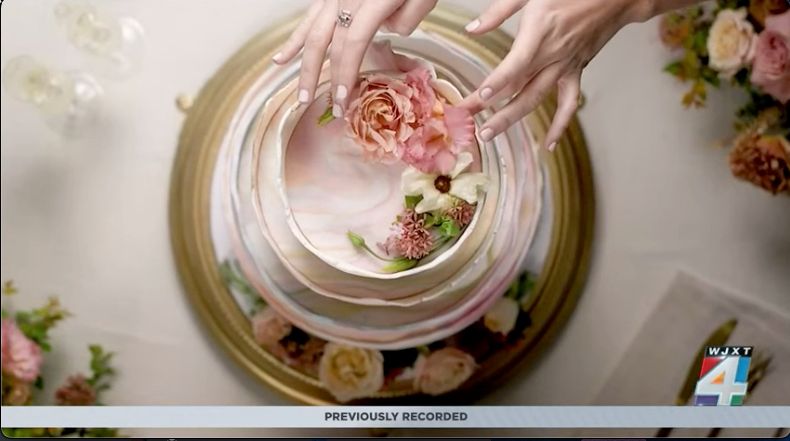 News4Jax WJXT segment on the micro wedding trend — hands styling a floral cake surrounded by garden roses