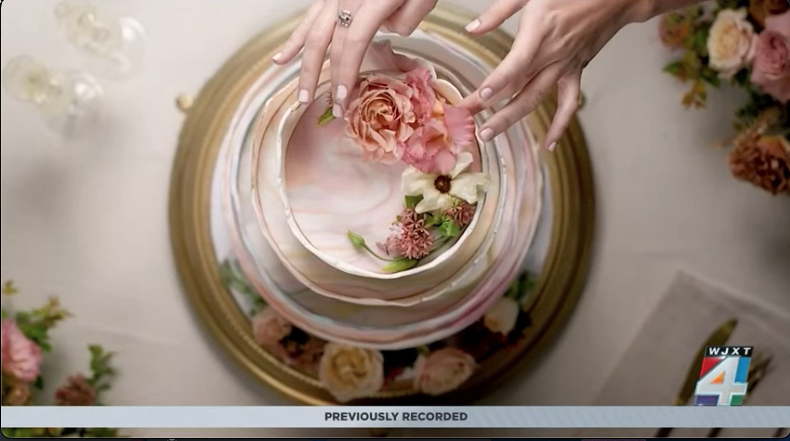 News4Jax WJXT segment on the micro wedding trend — hands styling a floral cake surrounded by garden roses